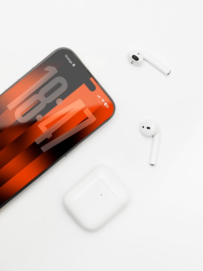 Minimalist setup of iPhone with AirPods on a white surface, showcasing modern technology.